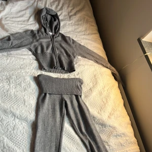 Grå croppad hoodie och byxa från Gina Tricot - Säljer ett set från Gina Tricot i grått med croppad hoodie och matchande byxa. Hoodien har dragkedja, huva och bred ribbad mudd vid midjan och ärmslut. Byxan har bred ribbad midja och är i mjukt stickat material.