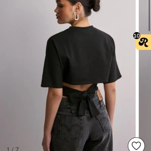 Svart croppad topp med rosett i ryggen - Trendig svart croppad topp med korta ärmar och snygg rosettdetalj i ryggen. Perfekt för dig som vill ha en stilren men ändå unik look. Toppen har en rak passform och är tillverkad i mjukt bomullsmaterial.