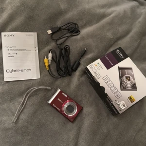 Sony Cyber-shot DSC-W370 digitalkamera röd - Säljer en röd vintage Sony Cyber-shot DSC-W370 digitalkamera med 14,1 megapixlar och 7x optisk zoom. Kameran har en stor LCD-skärm, levereras med originalkartong, manual, laddare, AV-kabel, 2GB SD-kort och batteri. Perfekt för dig som vill ha en smidig och snygg kompaktkamera.