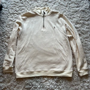 Vit halvzip-tröja från Polo Ralph Lauren - Säljer en stilren vit långärmad halvzip-tröja från Polo Ralph Lauren. Tröjan har en hög krage med dragkedja och den klassiska broderade loggan på bröstet. Perfekt för en clean och avslappnad look.