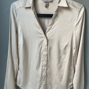 Satin skjorta från H&M🫶🏼 - Säljer just nu denna stilrena, cremévita skjortan från H&M med klassisk krage och knäppning framtill. Skjortan har lång ärm och är tillverkad i ett mjukt, lätt glansigt, satin material som ger en elegant känsla. Perfekt nu till våren/sommaren!🌸(Endast använd ett fåtal gånger, säljer pga inte använder längre.✨)