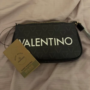 Svart axelväska från Valentino - Snygg svart helt ny axelväska från Valentino. Väskan har medföljande kort och lång axelrem samt en valentino dustbag. Väskan är aldrig använd med prislapp på och extra tillbehör ligger i originalförpackningen.