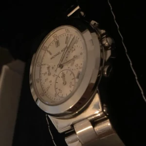 Silverfärgad klocka från Michael Kors - Klockans ny pris är 2650 kr så jag säljer den för ett väldigt attraktivt pris. Stilren klocka i silver med länkarmband och vit urtavla. Klockan har kronograf-funktion och tydliga markeringar samt datumvisning. Perfekt accessoar för dig som gillar klassisk design.
