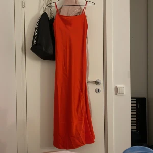 Orange långklänning från Kappahl - Säljer en snygg orange långklänning från Kappahl med smala axelband. Klänningen har en enkel och stilren design, perfekt för sommarens alla tillfällen. Materialet känns mjukt och följsamt mot kroppen. Prislappen kvar