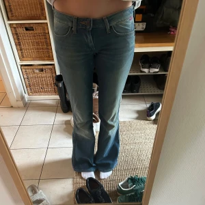 Blå bootcut jeans från Wrangler - Säljer ett par klassiska blå bootcut jeans från Wrangler med fem fickor och snygga sömmar på bakfickorna. Jeansen har normal passform och är tillverkade i denim. 