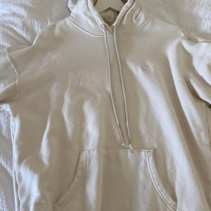 Beige hoodie från Adidas - Säljer en stilren beige hoodie från Adidas med broderad logga på bröstet. Tröjan har huva med dragsko och en stor magficka. Perfekt för en avslappnad och sportig look.