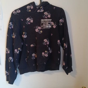 Svart hoodie med blommigt mönster från H&M - Mysig svart hoodie från H&M med blommigt mönster i rosa och lila toner. Tryck på bröstet med texten 'FRIENDSHIP FOREVER'. Tröjan har huva och magficka, samt långa ärmar och ribbade muddar. ❤️