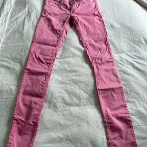 Säljer ett par rosa jeans från Replay. Byxorna har klassisk femficksdesign, dragkedja och knapp framtill samt smal passform. Perfekta för dig som vill sticka ut med färg i vardagen.