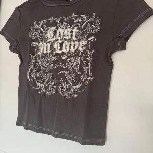 Mörkgrå t-shirt med tryck - Snygg tajt mörkgrå t-shirt med vit text. T-shirten har korta ärmar och rund halsringning.