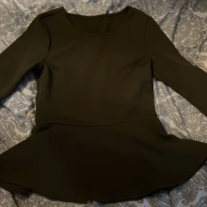 Olivgrön topp från Bik Bok - Säljer en olivgrön topp från Bik Bok med trekvartärmar och rund halsringning. Toppen har en figurnära passform upptill och en utställd kjol som ger en fin siluett. Perfekt för dig som gillar enkel och stilren design. Vet ej storleken men skulle gissa på M.