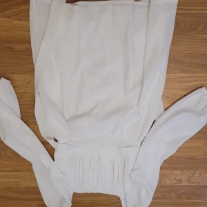 Vit långärmad klänning med smock i midjan - Säljer en söt vit klänning med långa ärmar och smockad midja. Klänningen har en luftig känsla och är perfekt för vår och sommar. Enkel och stilren design som passar till många tillfällen.