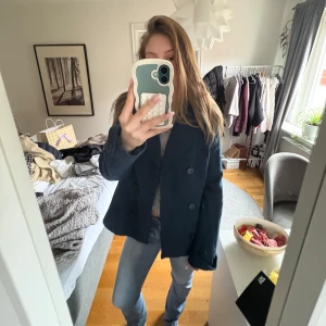 Mörkblå kappa med knappar - Säljer en mörkblå kappa med klassisk krage och dubbelknäppning framtill. Jackan har lång ärm och är perfekt för dig som vill ha en stilren och tidlös look.