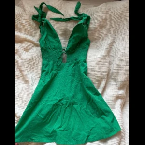 Grön kort klänning med knytband - Kort klänning med knytband på axlarna och v-ringad urringning. Klänningen har smockad midja, liten slits framtill och är ärmlös.💚 Jag är 166 cm och bär storlek S!