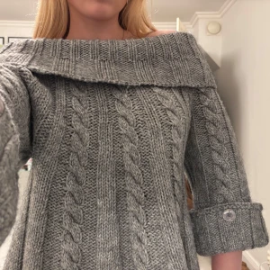 Grå stickad offshoulder - Superfin grå stickad tröja med bred offshoulderkrage. Tröjan har trekvartsärmar med stora uppvik och dekorativa knappar. Sitter löst så kan passa många! Sitter bara åt vid axlarna. 15%ull 15%mohair