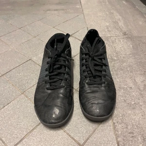 Svarta fotbollsskor från Puma - Säljer ett par svarta fotbollsskor från Puma med diskret mönster och snörning. Skorna har en låg profil och platt sula, perfekt för spel på inomhusunderlag. Klassisk design med Puma-logga undertill. Nytt pris 699 Mitt pris 300