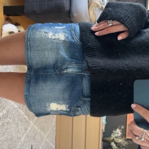 Blå jeanskjol med slitningar - Säljer en blå jeanskjol med coola slitningar framtill. Kjolen har klassiska fickor och knappstängning. Perfekt för dig som gillar en avslappnad och trendig stil.