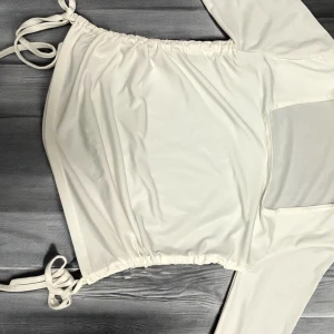 Vit långärmad topp med knyt från Dispatch - Säljer en vit långärmad topp från Dispatch med knyt i sidorna och lätt croppad passform. Toppen har en enkel design och är tillverkad i ett mjukt syntetmaterial. Perfekt att styla med jeans eller kjol! Står L som storlek men är väldigt tajt. Skulle nog passa bäst för Xs, S, och M. 