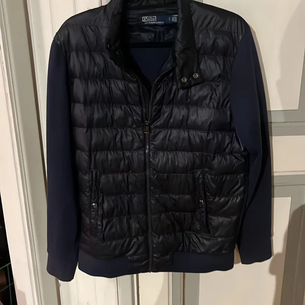 Snygg mörkblå jacka från Polo Ralph Lauren med quiltad front och släta ärmar. Jackan har dragkedja, ståkrage och två fickor framtill. Perfekt för dig som vill ha en stilren och sportig look.. Takit.