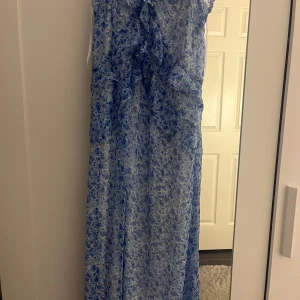 Blå klänning  - Säljer en luftig långklänning från Vero Moda i blått och vitt blommönster. Klänningen är ärmlös och har volangdetaljer framtill. Perfekt för varma dagar och somriga tillfällen.