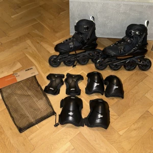 Svarta inlines från Roces med skydd - Säljer ett par svarta inlines från Roces tillsammans med ett komplett set skydd (knä, armbåge, handled) i matchande svart. Inlinesen har snörning och spänne för extra stabilitet och sitter bekvämt på foten. Perfekt för dig som vill börja åka inlines.