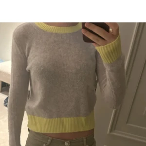 From Future tröja - Säljer en grå stickad tröja med ribbade gula muddar vid hals, ärmslut och nederkant. Tröjan har en klassisk rund halsringning och lång ärm. Perfekt för dig som gillar en enkel men färgglad look. Super fint skick och materialet är toppen. Perfekt om du gillar Stockholm stil.