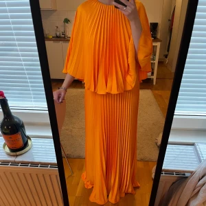 Plisserad långklänning i orange - Säljer en jättefin orange maxiklänning med plisserat tyg. Den är perfekt till bal eller liknande! Den är helt oanvänd med prislapp kvar. Den är i storlek M. Kan mötas upp i Uppsala vid köp💕💕