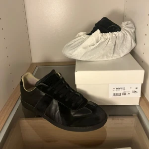 Svarta Maison Margiela gats - Maison Margiela gats  sneakers i helsvart med ovandel i skinn och mocka. Klassisk låg modell med rund tå och platt sula. Diskret beige insida och svarta skosnören. Skorna kommer med sko box och dust bag. Skicket på skorna är 8/10 pga sulan.