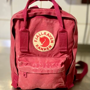 Röd Kånken Mini ryggsäck från Fjällräven - Säljer en klassisk röd Kånken Mini ryggsäck från Fjällräven. Väskan har ett stort huvudfack, en mindre ficka framtill med dragkedja och två sidofickor. Ikonisk rund logotyp på framsidan och justerbara axelremmar.Se mer på bilden,