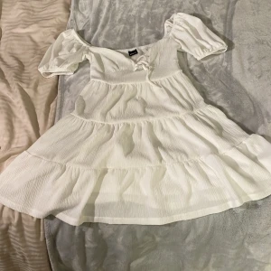 Vit omlottklänning med puffärm från Gina Tricot - Superfin vit klänning från Gina Tricot med puffärmar och omlottdetalj framtill. Klänningen har en lätt rynkad struktur, volang i kjolen och knytning vid bysten. Perfekt för sommarens alla tillfällen!