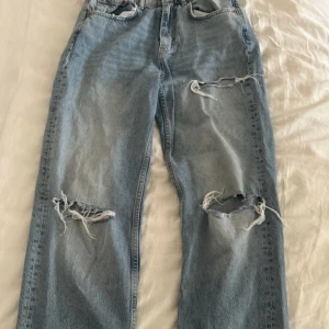 Ljusblå slitna baggy jeans från Gina Tricot - Ljusblås baggy jeans med raka ben och stora slitningar på båda benen och en mindre slit på ena benet. Klassisk femficksmodell med normal passform och hög midja. 