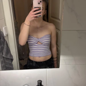 Randig tubtopp i lila och vit - Säljer en snygg randig tubtopp i lila och vit med en twistdetalj framtill. Toppen är ärmlös och croppad, perfekt för sommardagar. 