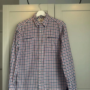 Rutig skjorta från Lexington - Säljer en snygg rutig skjorta från Lexington i storlek medium. Skjortan har ett klassiskt rutmönster i blått, rött och vitt med långa ärmar och knappar framtill. Perfekt för en stilren look! Storlek M