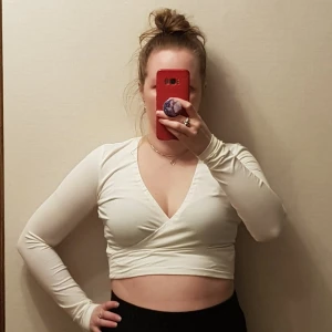 Vit croptopp från Gina Tricot strl S - Säljer en stilren vit croptopp från Gina Tricot i ekologisk bomull. Toppen med långärmade ärmar och en v-ringad design. Perfekt för en trendig look! Har syt in ett elastiskt band i urringnenden för att hålla den på plats den har också en omlått look