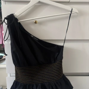 Svart one shoulder topp från Zara - Säljer en svart one shoulder topp från Zara med smockad midja och gula ränder. Storlek S. Säljer för 120kr, är öppen för andra priser!!