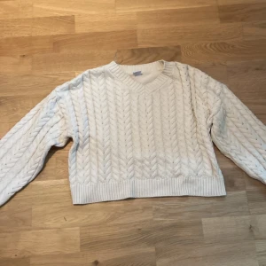 Vit/ beige stickad tröja från Lindex - Säljer en mysig vit/beige stickad tröja från Lindex med ett klassiskt flätmönster. Tröjan har en v-ringad hals och långa ärmar med ribbade muddar. Perfekt för kyliga dagar!
