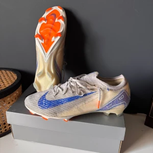 Nike mercurial vapor 16 elite  - Snygga fotbollsskor från Nike med en stilren design i grått och blått. Skorna har en iögonfallande blå Nike-logga och orange detaljer på sulan. Perfekta för fotbollsplanen med sin snörning och rund tå. bra skick för bra pris. Storlek 45. 