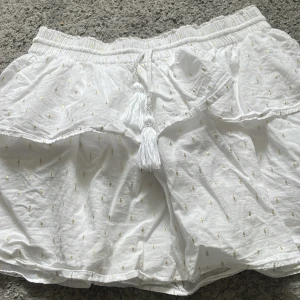 Vit kjol från Gina Tricot - Vit kjol med band som man kan spänna in med och gulddetaljer. Väljer att sälja pga av att jag använder silver smycken.