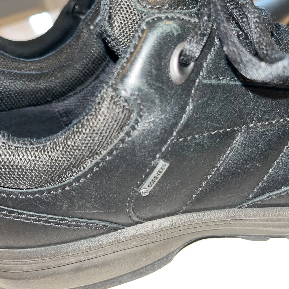 Snygga svarta sneakers från Ecco med snörning och Gore-Tex-material för extra skydd mot väta. Skorna har en robust sula med röd detalj för bra grepp och komfort. Perfekta för vardagsbruk och håller dina fötter torra och bekväma.. Kengät.