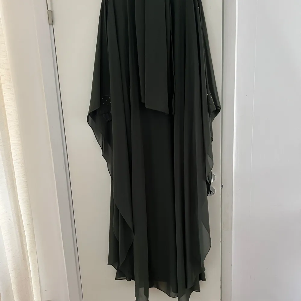 Elegant mörkgrön kaftan med vackra guldfärgade broderier och pärldetaljer framtill. Den har en lös passform och vida ärmar, perfekt för en sofistikerad look.. Mekot.