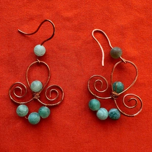 Handgjorda örhängen med gröna pärlor och koppartråd - Unika örhängen i form av snirkliga fjärilar, tillverkade av kopparfärgad metalltråd och dekorerade med gröna och ljusgröna pärlor. Perfekta för dig som vill sticka ut med ett personligt smycke.