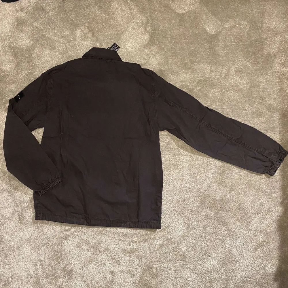 Säljer en svart vindjacka från Stone Island med klassisk logotyp på ärmen. Jackan har dragkedja framtill, bröstficka med knapp och ståkrage. Perfekt för dig som gillar stilrena och funktionella plagg.. Takit.