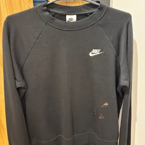 Svart sweatshirt från Nike - En svart sweatshirt från Nike med klassisk logga på bröstet. Tröjan har rund halsringning och långa ärmar. Tillverkad i mjukt bomullsmaterial, perfekt för en avslappnad stil. Den har lite fläckar på magen.