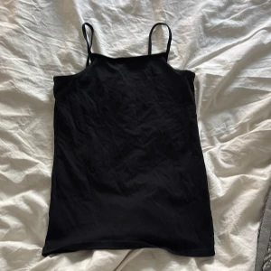 Svart linne från H&M - Ett enkel svart linne  från H&M med smala axelband. Linnet har en rak passform och är tillverkad i mjukt material, perfekt för sommardagar eller som basplagg. Stilren och lätt att matcha med olika accessoarer. Säljer en likadan i grå 
