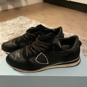 Svarta sneakers från Philippe Model - Snygga svarta sneakers från Philippe Model med en stilren design. Skorna har snörning och en rund tå, med en kombination av skinn och mocka i materialet. Perfekta för en trendig look. Skorna är 8:10 box och allt ingår.
