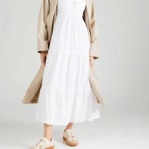 Vit långklänning med smock och axelband - Helt ny med prislapp Superfin vit långklänning med smock upptill och smala axelband. Klänningen har en luftig och flowy passform med volangdetaljer i kjolen. Perfekt för varma dagar och somriga tillfällen. Enkel och stilren design som är lätt att matcha.