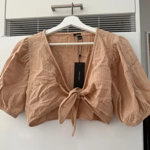 Beige knytblus från Vero Moda - Säljer en snygg beige blus från Vero Moda med knytning framtill. Perfekt för en stilren och somrig look. Prislappen kvar bara testad. Storlek M men är som en S