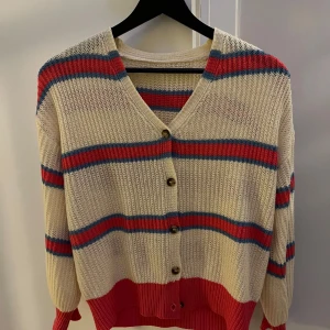 Randig kofta med knappar XS/S - Fin randig kofta med v-ringning och knappar framtill. Koftan har en beige bas med rosa och blå ränder. Ganska tunn.