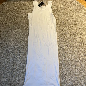 Vit långklänning i bomull - Säljer en enkel och stilren vit långklänning i bomull. Klänningen är ärmlös med rund halsringning och har en rak passform som passar perfekt till sommaren. Superskön och lätt att styla med accessoarer.