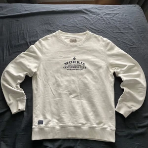 Vit sweatshirt från Morris - Säljer en stilren vit sweatshirt från Morris med trycket 'Gentlemens Club' på bröstet. Tröjan har rund halsringning, långa ärmar och ribbade muddar vid ärmslut och nederkant. Perfekt för en clean och klassisk look.