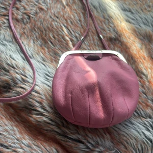 Rosa axelväska med metallram - Säljer en söt rosa axelväska med en elegant metallram och lång axelrem. Väskan har en unik form och är perfekt för att bära med sig det nödvändigaste. Den är både stilren och praktisk.